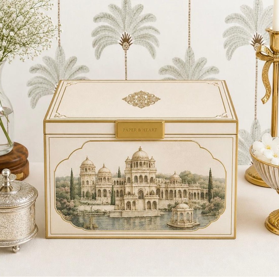 A cream and gold invitation box painted with a lakeside palace